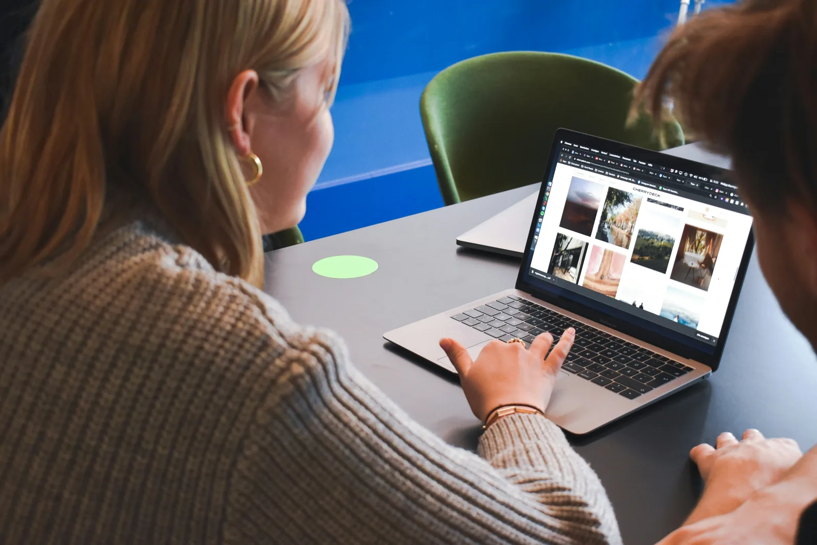 People sit at a table, viewing a laptop displaying a grid of photo thumbnails.